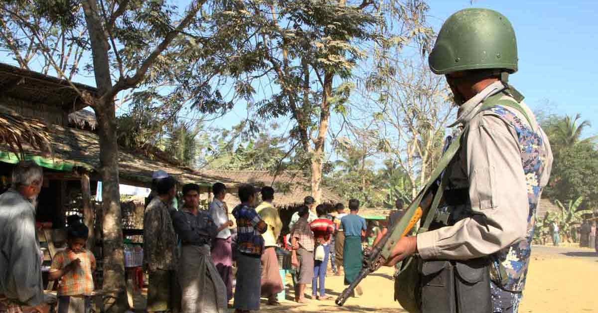 This file photo shows a Myanmar border guard policeman standing near a group of Rohingya Muslims in front of their homes in a village as seen during a government-organised visit for journalists in Buthidaung townships in the restive Rakhine state on 25 January 2019. (AFP Photo)