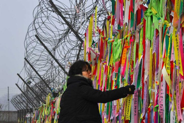 A woman looks at ribbons hanging from a military barbed wire fence calling for peace and reunification at the Imjingak peace park in the border city of Paju near the Demilitarized Zone (DMZ) dividing the two Koreas