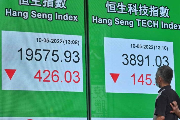 A man passes a board displaying the Hang Seng Index