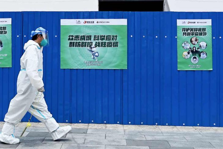 A health worker wearing PPE walks past a fenced residential area under lockdown in Beijing